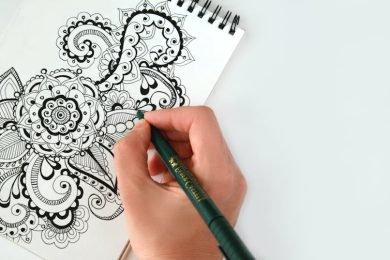 Close-up of a hand drawing an intricate mandala pattern on a sketchbook using a pen. Perfect for creativity themes.